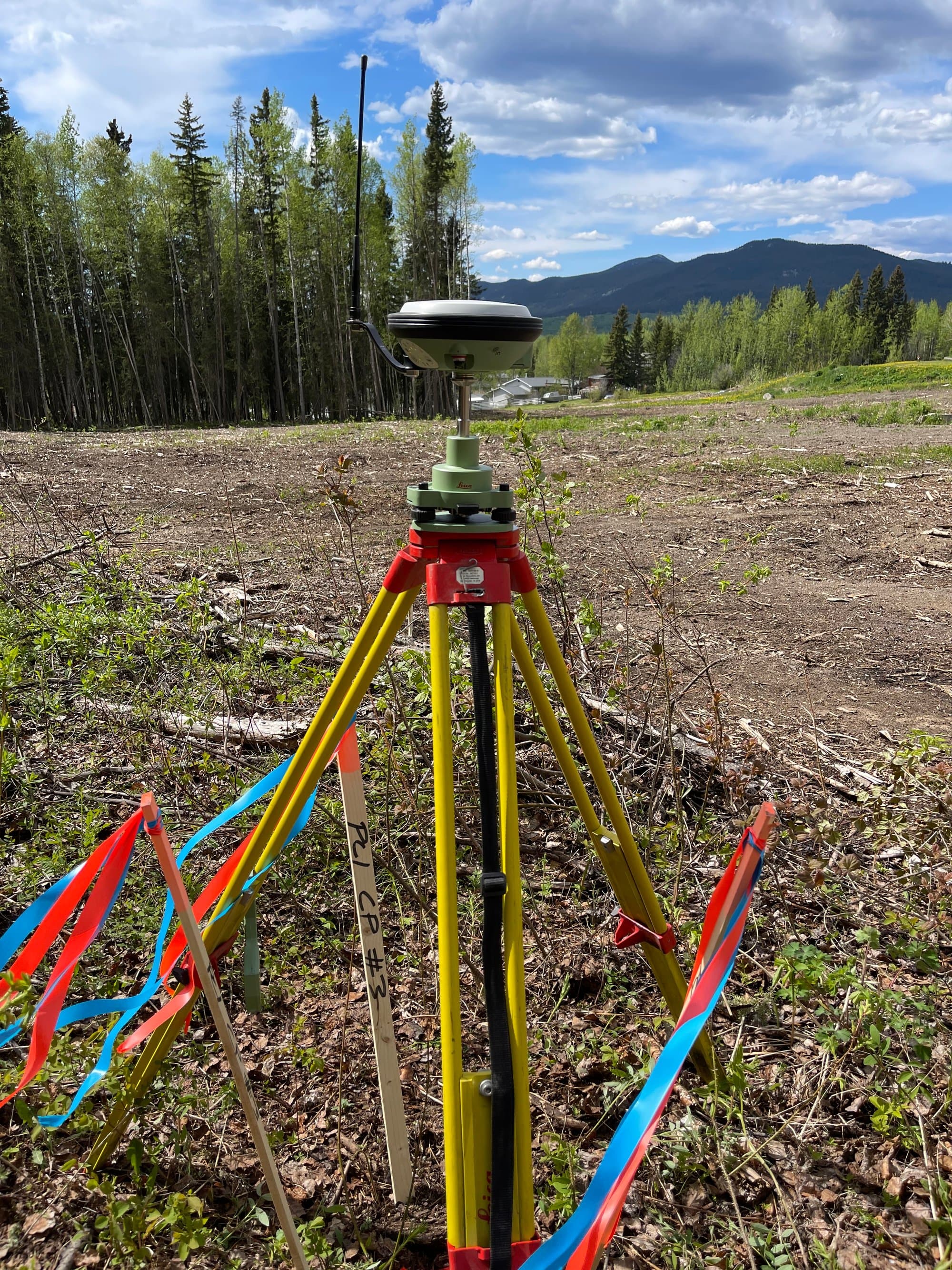 GNSS base station and layout stakes on a cleared site with mountains behind