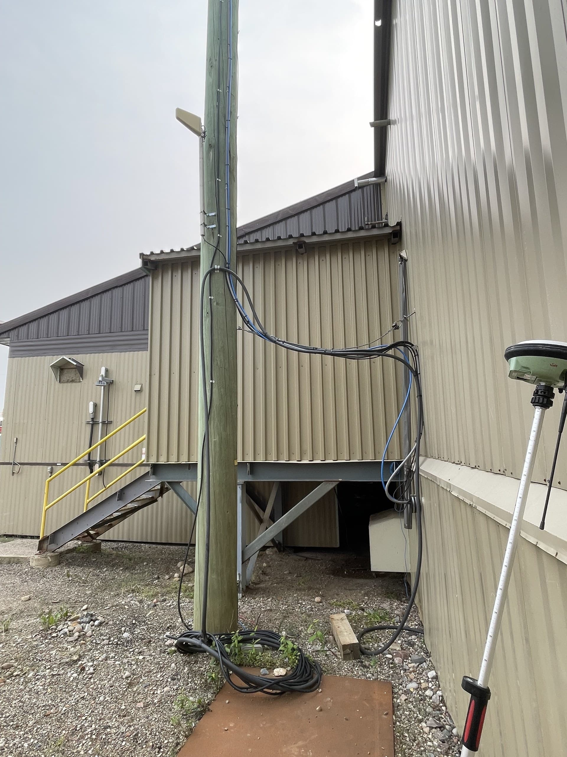 GNSS rover pole beside a utility building and cabled pole