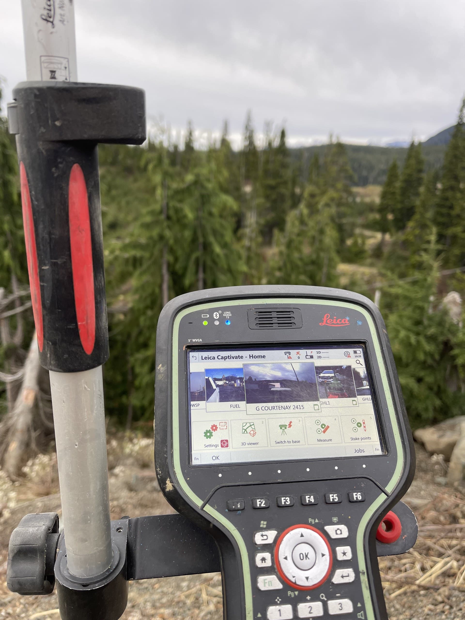 Field controller on a rover pole with a Courtenay job open on screen, second-growth forest behind