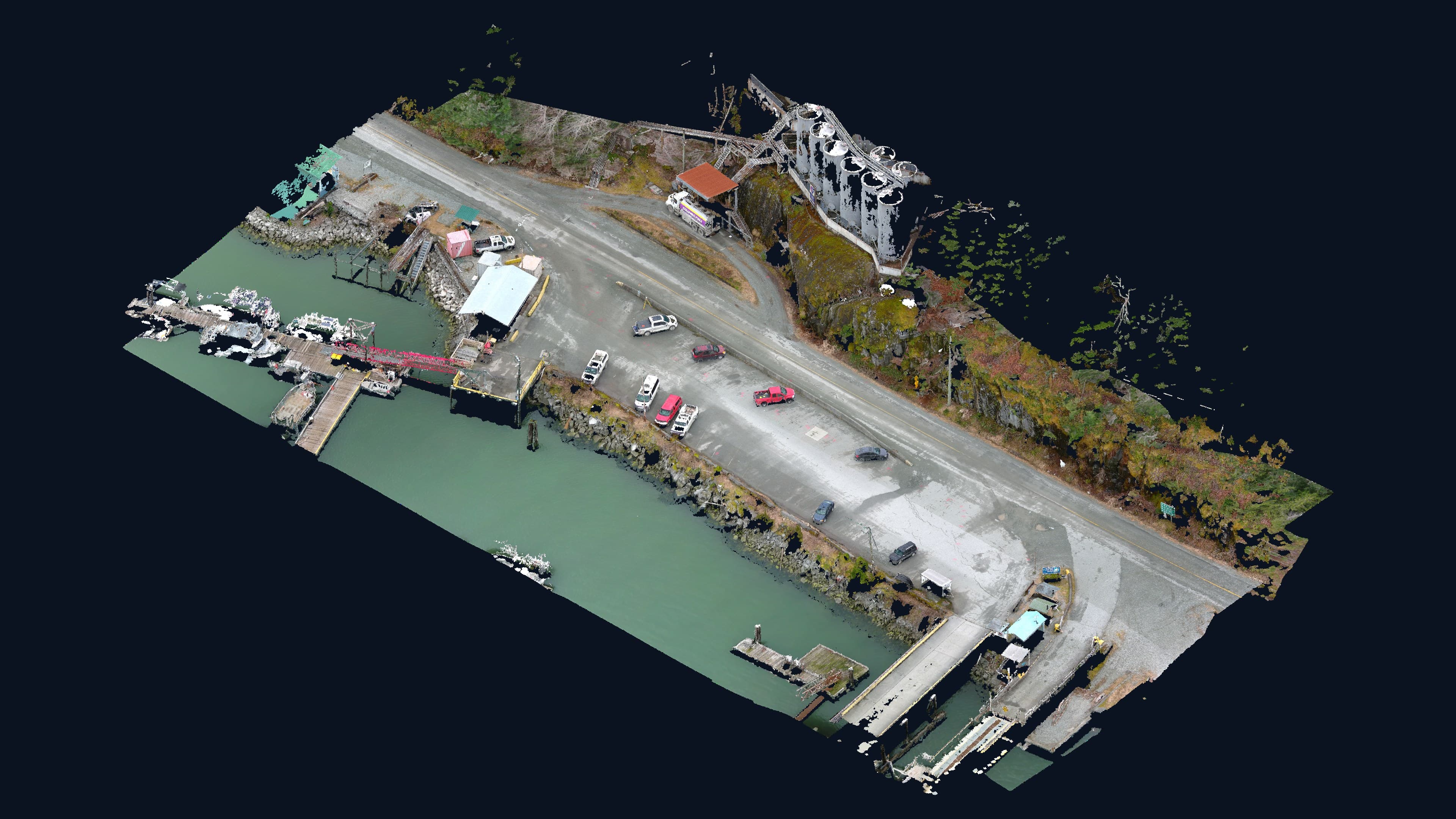 Colourized LiDAR point cloud of a working waterfront: fuel tanks on a rock bluff, a highway, wharf, boats and green water