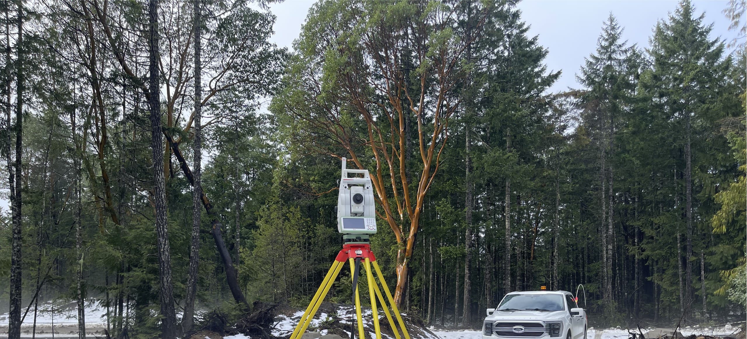 Robotic total station on a snowy Vancouver Island clearing beside an arbutus tree